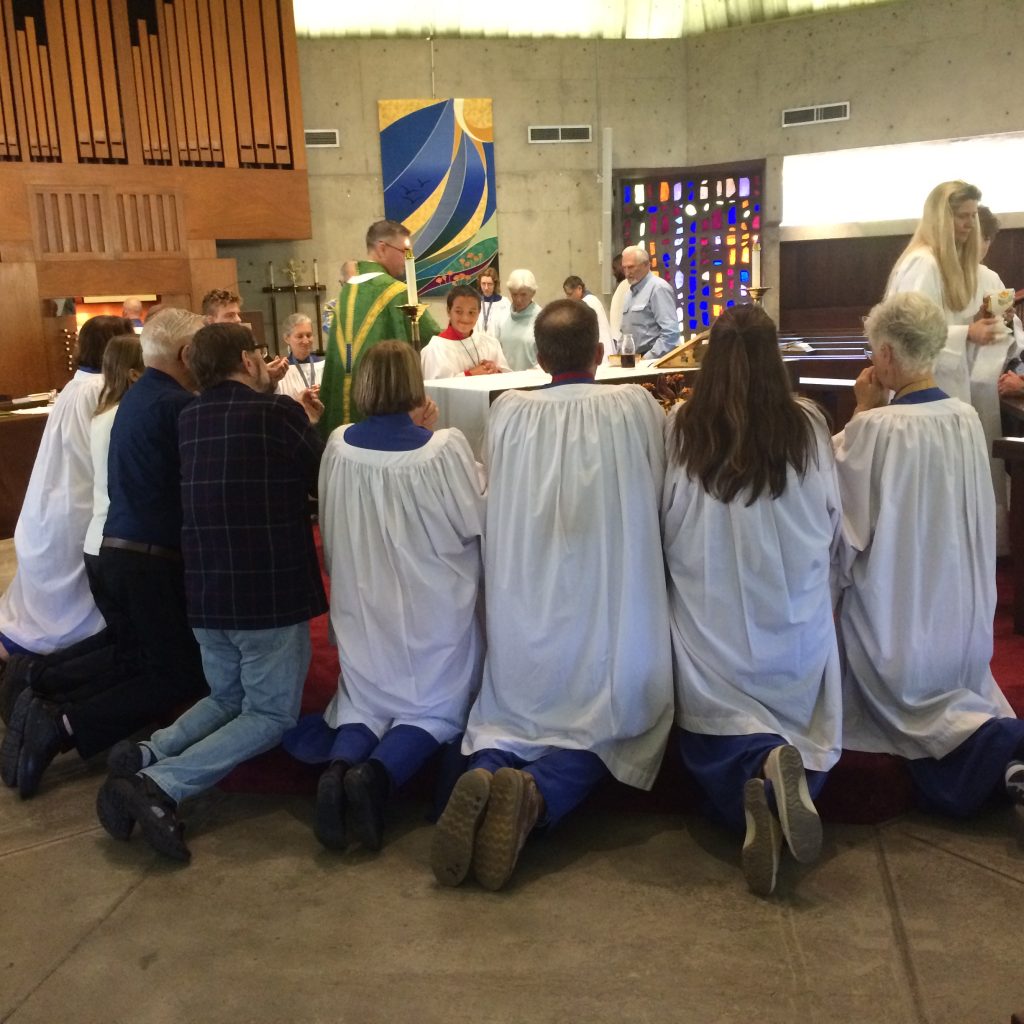 A group of people in choir roles kneeling for Eucharist at a round altar.