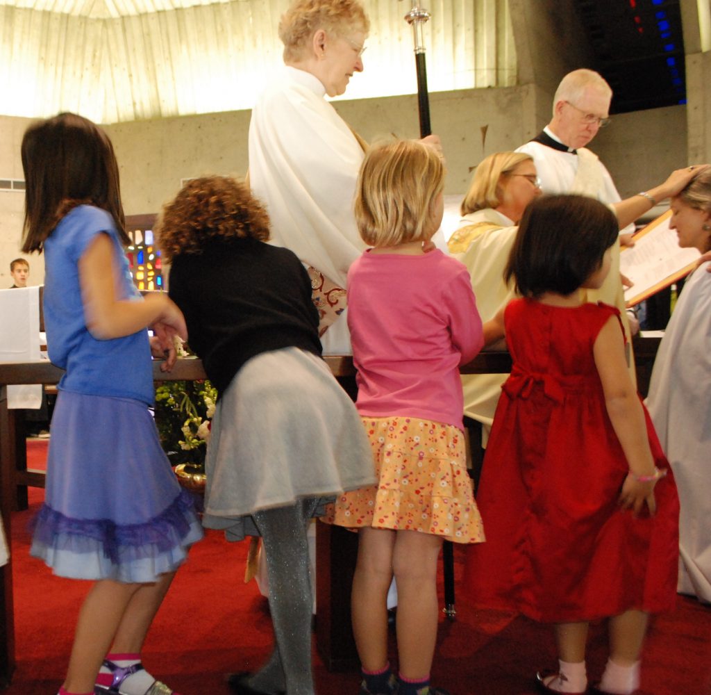 A group of 4 children waiting for Eucharist at a round altar.